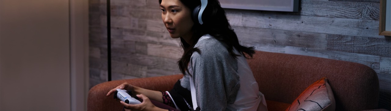  一位女性頭戴著耳機，手持Playstation手柄，沉浸在她的娛樂世界中。