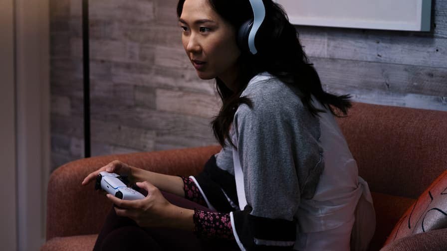  一位女性頭戴著耳機，手持Playstation手柄，沉浸在她的娛樂世界中。