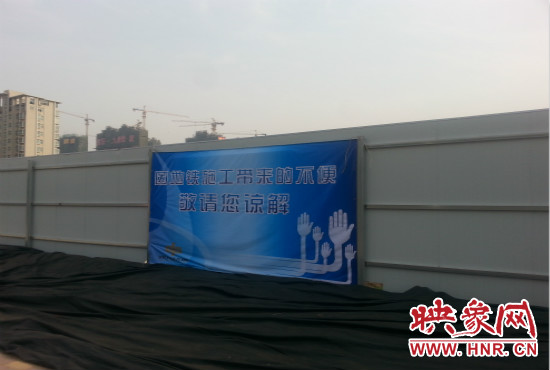 道路南側(cè)圍起了白色的圍擋，墻上標(biāo)示著“因地鐵施工帶來的不便敬請您諒解”的提示牌。